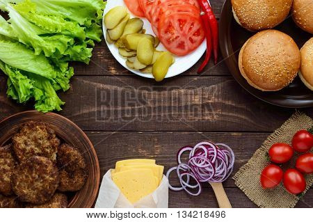 Ingredients for making hamburgers (bread rolls tomatoes cucumbers onion rings lettuce pork chops cheese) on wooden background. top view