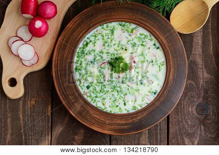 Slavonic traditional dish - cold soup "okroshka" in the yogurt in a clay bowl on a wooden background. Dietary refreshing dish. The top view