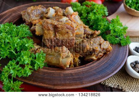 Pork ribs steamed with carrots parsley decorated in a clay bowl on a wooden background. Close up