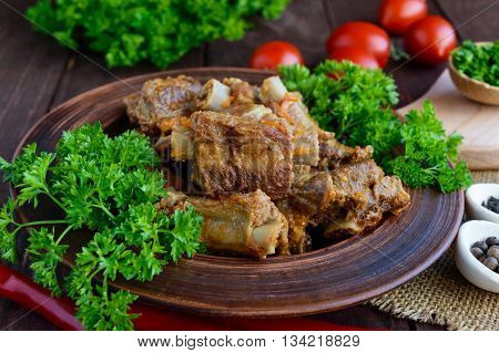Pork ribs steamed with carrots parsley decorated in a clay bowl on a wooden background. Close up