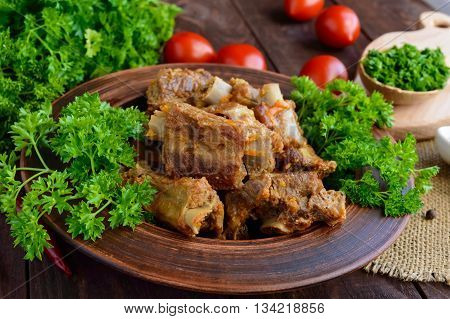 Pork ribs steamed with carrots parsley decorated in a clay bowl on a wooden background. Close up