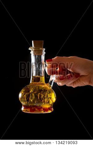 Bottle of olive oil with fresh herbs in a hend on black background.