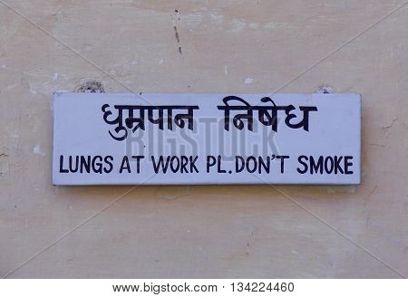 No smoking sign in English and Hindi on a wall requesting politely and humorously that nobody smokes in that public area.