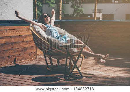 Enjoying carefree time. Beautiful young woman relaxing in a big comfortable chair on her outdoor house terrace