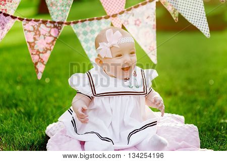 happy little girl sitting on the grass with flags on the background.