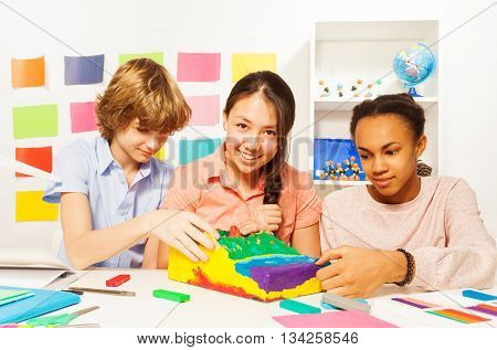 Three multi ethnic students modeling surface relief with plasticine at the geography lesson