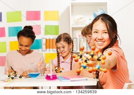 Four multi ethnic students researching chemical process with molecular model and reagents at the laboratory