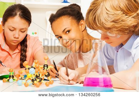 Three multi ethnic students writing chemical formula sitting at the desk in science class