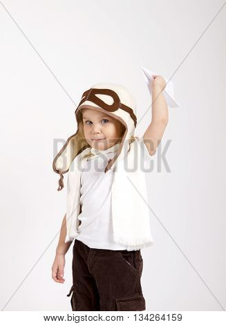 happy kid playing with paper airplane. studio photo. aviator hat and scarf