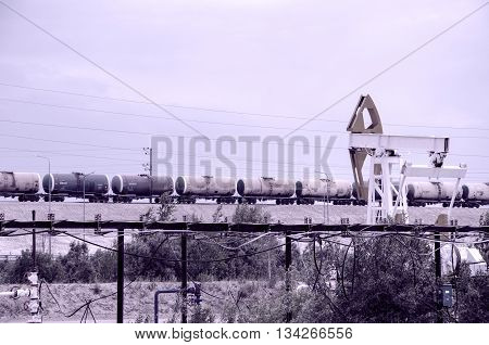 Pump jack well head and pipeline on the background of tank train. Oil and gas concept. Toned.
