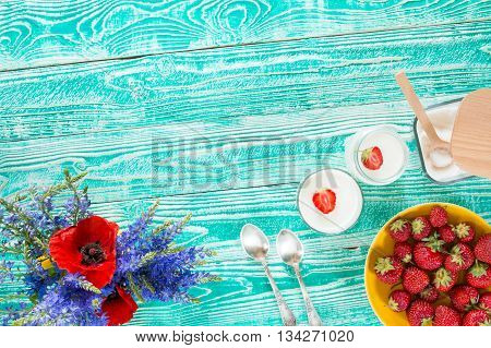 yogurt in glass jars strawberry sugar bowl flowers wooden spoons on turquoise colored wooden table top view