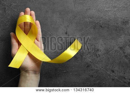 Hand holding yellow ribbon on dark background