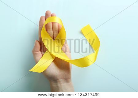 Hand holding yellow ribbon on light grey background