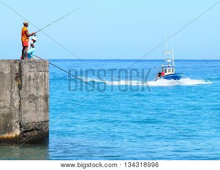 SAINT-PAUL, REUNION ISLAND, FRANCE - NOVEMBER 11, 2015: Unidentified african fishermens catching a fish in harbor. Traditional leisure activity for natives on Reunion. 