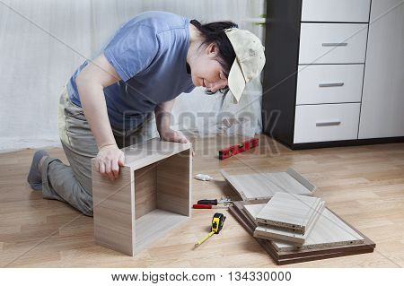 Woman connects together the board chipboard drawer assembly of furniture at home.