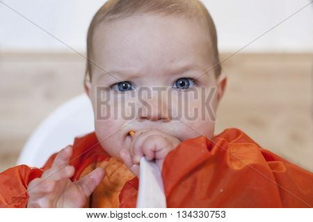 8 month baby boy having his cereal mush. He is wearing an orange bib. Trying to eat independently