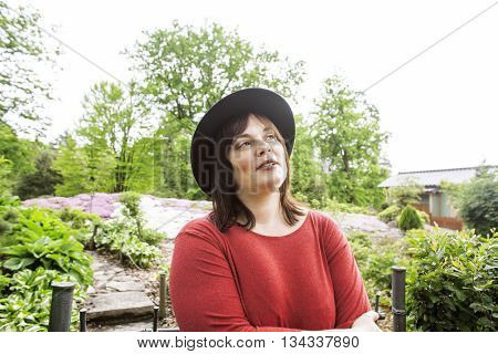 mature brunette fat woman in green garden wearing hat, smiling, friendly welkoming, lifestyle people concept close up