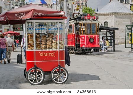 ISTANBUL TURKEY - JUNE 5 2016: The nostalgic tram pulling up beside a cart selling traditional Turkish simit bread at the Taksim Square end of the famous Istiklal Caddesi street. Tourists and locals enjoy the sunshine on a summer morning.
