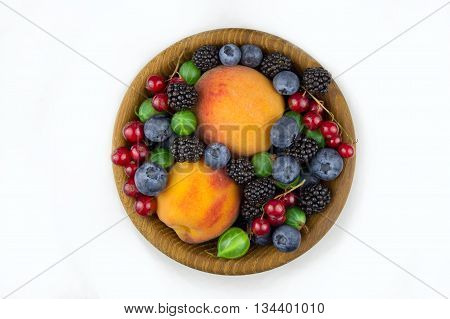 fruits and berries in a wooden plate gooseberries blackberries peaches blueberries