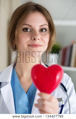 Female medicine doctor hold in hands red toy heart closeup. Cardio therapeutist physician make cardiac physical heart rate measure or arrhythmia concept