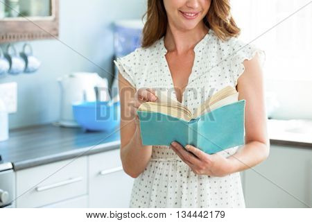 Mid section of young woman reading book in kitchen at home