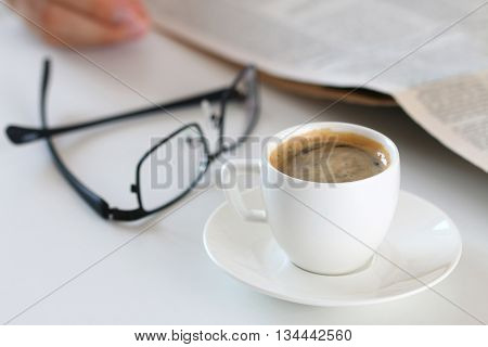 Cup of morning coffee on worktable with glasses and newspaper on background. Price quotation on the exchange relaxing at workplace or football match result concept