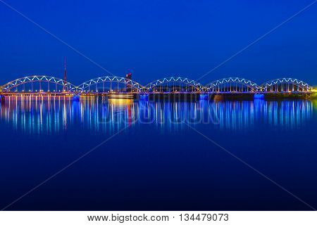 Illuminated Railway Bridge And Reflection In Daugava River At Twilight. Riga, Latvia
