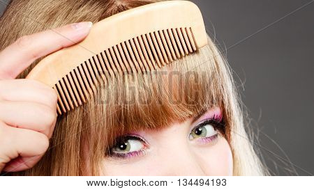 Fashion beauty and haircare concept. Closeup young woman refreshing her hairstyle girl combing her hair fringe with wooden comb