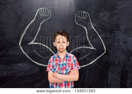 Portrait of little boy on backgroung of blackboard with drawn muscles
