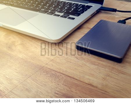 External or portable hard drive (HDD) connected to laptop computer for transfer or backup data on wooden texture office desktop with copy space