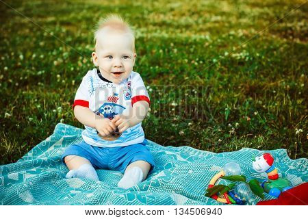 Cute funny baby sitting on a blanket on the grass and smiling