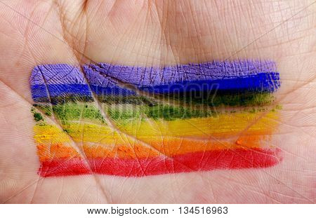 closeup of the palm of the hand of a young caucasian man with a rainbow flag painted in it