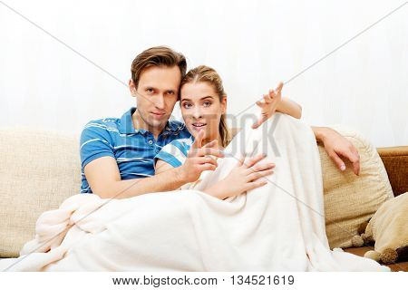 Smiling loving couple sitting on couch with blanket