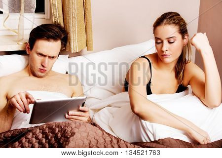 Couple in bed-man reading woman sitting sad
