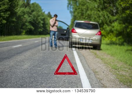 Red triangle warning sign closeup man calling to a car assistance after breakdown. Selective focus
