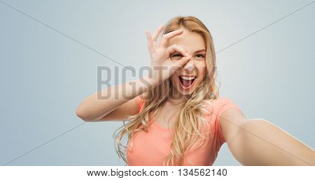 emotions, expressions and people concept - happy smiling young woman taking selfie over gray background