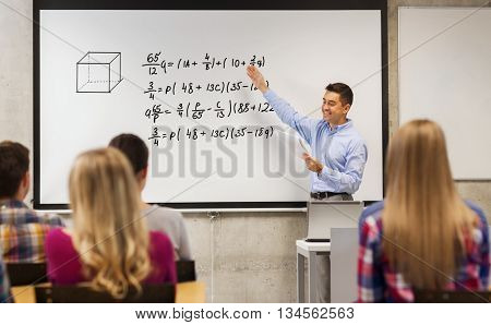 education, high school, mathematics and people concept - smiling teacher with notepad standing in front of students and showing mathematical equalities on white board in classroom