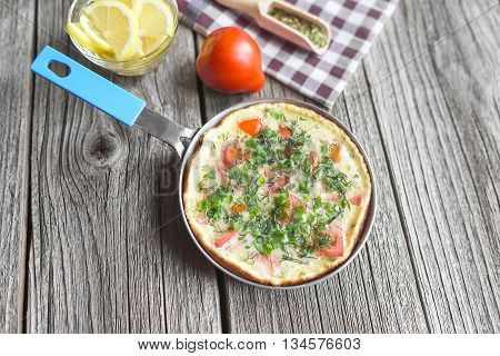 Omelet with vegetables in a frying pan on a wooden table.