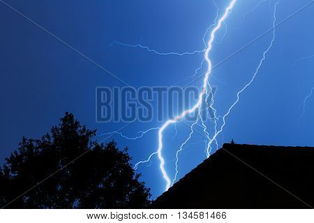 Lightning striking in the city with house and tree in blue sky