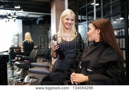 Young hairdresser with hair spray fixating client hairdo at beauty salon