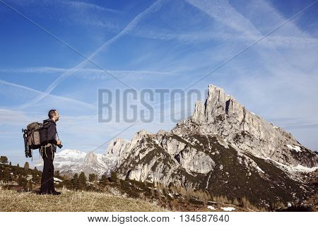Hiker photographer on a mountain top admiring the surrounding alpine landscape enjoying the view. Active lifestyle natural environment freedom and sports concept. Big blue sky in the background.