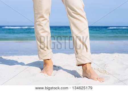 Close-up Of Female Legs In Beige Pants Barefoot On The Beach