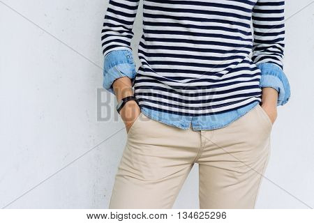 Close-up of a woman in a denim shirt striped t-shirt and beige pants with a fitness tracker at hand the details of women's clothing