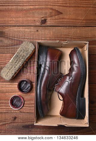 A pair of shoes in a shoebox with polish and brush on a dark wood floor. Vertical format with copyspace, seen form a high angle.