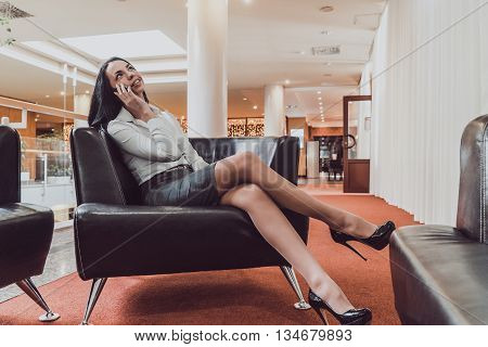 Stylish girl talking on a smartphone sit on a sofa in the hall of the hotel