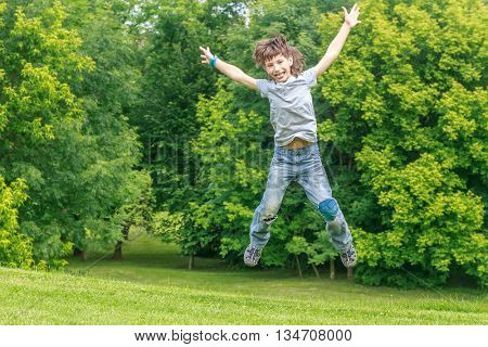 Adorable young child boy in the park. On warm summer day during school holidays. Kid boy jumping and smiling.