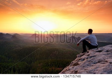 Adult In Black Trousers, Jacket Sit On Cliff's Edge