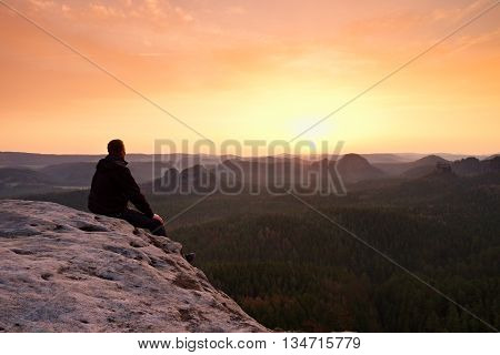 Adult In Black Trousers, Jacket Sit On Cliff's Edge