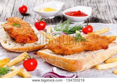 sandwich with ciabatta and Bread Crumb Coated fried pork chop with french fries red onion cherry tomatoes and dill on a parchment paper studio lights view from above close-up