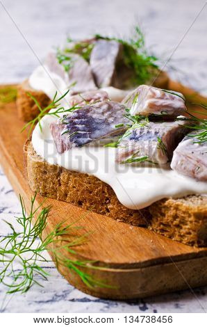 Sandwich with pieces of marinated herring with cream and dill. Selective focus.